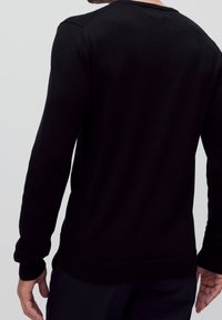 Maglione nero realizzato in morbido tessuto, con maniche lunghe, polsini e orlo a costine, dal design semplice e pulito. Nessun motivo o decorazione.