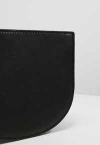 Sort læderhåndtaske med en buet, halvmåneform, glat tekstur og minimal syning langs kanterne.