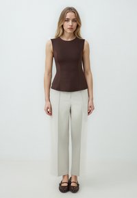 Top aderente senza maniche color marrone, abbinato a pantaloni larghi grigi chiari. L'insieme presenta texture morbide e linee di design sottili.