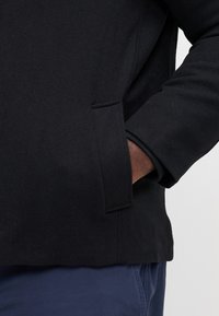 Black fleece jacket with a slim fit, featuring a front pocket and rolled cuffs. Soft texture with minimal stitching details.