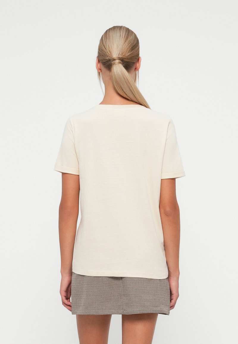 Camiseta de color crema con mangas cortas, corte relajado y un escote redondo simple, combinada con una falda a cuadros.