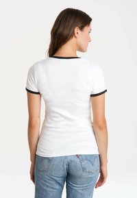 Weißes Baumwoll-T-Shirt mit marineblauen Akzenten am Kragen und an den Ärmeln, taillierte Passform und glatte Textur, kombiniert mit blauen Jeans.