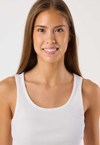 Valkoinen ribbineuloksinen toppi pyöreällä pääntiellä, jossa on istuva malli ja leveät olkaimet, päällä suoratukkaisella henkilöllä.