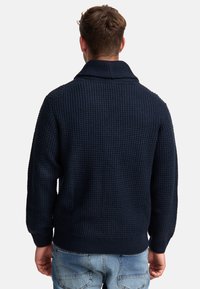 Suéter de punto azul marino con textura en relieve, cuello alto y puños de canalé. Presenta un corte holgado y un diseño casual.