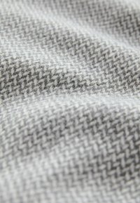 Geweven grijze stof met een houndstooth patroon, met een zachte, gestructureerde oppervlakte; mengsels van donkere en lichte grijstinten.