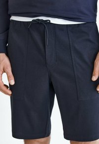 Shorts bleu marine en tissu léger avec une ceinture élastique, un cordon de serrage et deux poches latérales, présentant un design avant plat.