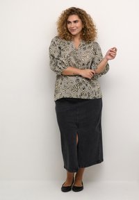 Bluse mit braunem und beigem Leopardenmuster, Dreiviertelärmel, kombiniert mit einem langen Jeansrock in Dunkelblau mit einem Schlitz in der Vorderseite. Schwarze Ballerinas.