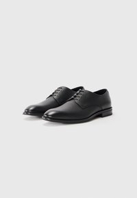 Zapatos formales de hombre de cuero negro con cordones, de acabado suave y ligeramente texturizado y tacones bajos apilados, sobre un fondo liso.