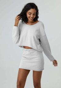 Cropped top grigio chiaro con maniche lunghe e scollatura rotonda, abbinato a una mini gonna con coulisse coordinata. Tessuto morbido, vestibilità comoda.