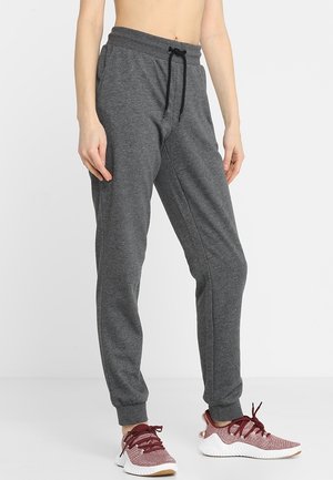 Osoba ubrana w ciemnoszare spodnie dresowe z czarnym ściągaczem i różowe buty sportowe z bordowymi sznurowadłami, stojąca na białym tle.