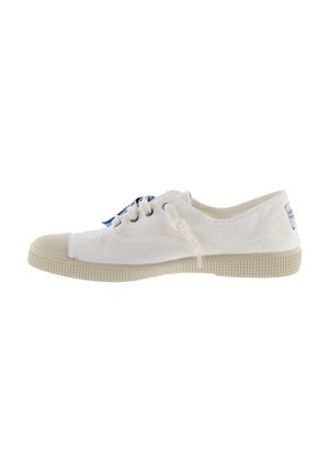 Zapatilla de lona blanca con una puntera de goma, cordones redondos y una suela texturizada. Presenta una etiqueta azul en el talón. Parte superior de tela suave.