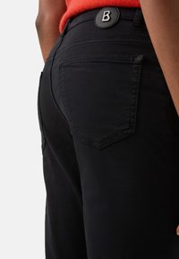Černé bavlněné kalhoty s přiléhavým střihem, vybavené zadními kapsami a kulatým černým knoflíkem s bílým logem "B" na pásku.