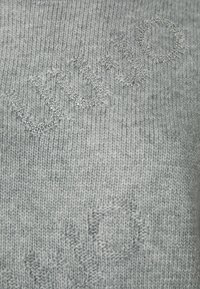 Suéter de punto gris con áreas texturizadas y adornos brillantes de pedrería que forman letras y patrones en la superficie del tejido.