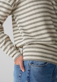 Beige striped sweater with black lines, ribbed texture, and fitted cuffs, paired with light blue denim jeans featuring classic pockets.