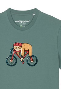 Mintgroene t-shirt met een cartoonluiaard die op een rode fiets rijdt, met zwarte wielen en een helm. Zacht materiaal en een ronde halsontwerp.