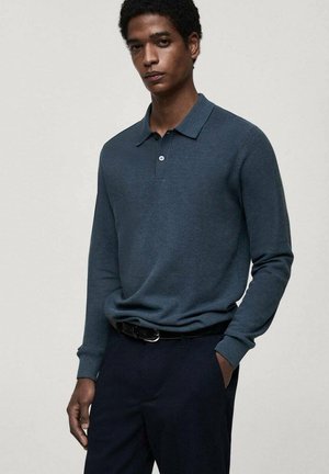 Polo a maniche lunghe di colore blu scuro con tessuto testurizzato, placca a tre bottoni e colletto classico, abbinato a pantaloni scuri.