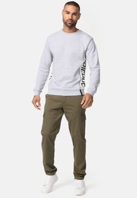 Sweatshirt gris avec logo noir sur le côté, col rond ; associé à un pantalon cargo vert olive avec poches latérales ; baskets blanches.