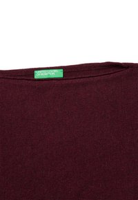 Collo di un maglione lavorato a maglia color mogano con un'etichetta verde che recita "UNITED COLORS OF BENETTON" su uno sfondo bianco.