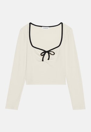 Långärmad croppad topp i ribbat krämfärgad tyg med svart kant, fyrkantig halsringning och veck i mitten med en knuten rosettdetalj.