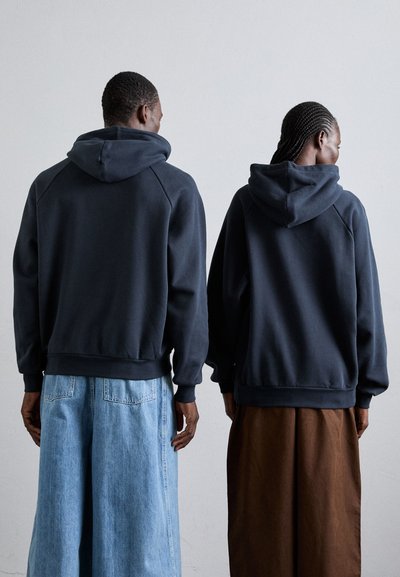 Sweatshirts à capuche de la marine en tissu doux avec des manches raglan. Un porteur les associe à un pantalon en denim large, l'autre avec une jupe fluide marron.