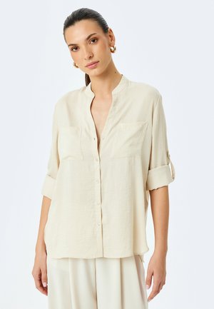 Crème-kleurig shirt met een Mandarin-kraag, twee voorzakken en opgerolde mouwen. Gemaakt van een lichtgewicht, gestructureerde stof.