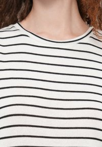 Top en maille rayé avec des rayures horizontales noires et blanches, un col rond, et un tissu doux et texturé.