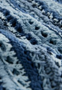 Häkeldecke in verschiedenen Blautönen und Türkis, mit einem offenen Webmuster und weicher Textur, die ein geschichtetes Aussehen erzeugt.