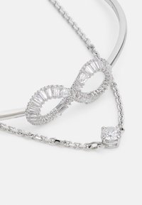 Collana in argento con un centro a forma di infinito adornato da pietre taglio baguette e una pietra trasparente rotonda su una catena.