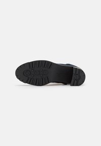 Suela de zapato de goma negra con patrón de agarre texturizado, que presenta tacos hexagonales, diseño plano y un ligero talón elevado para estabilidad.