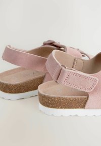 Roze suède sandalen met klittenbandsluiting, kurken voetbed en witte rubberen zool. Kenmerkt zich door afgeronde randen en minimale details.