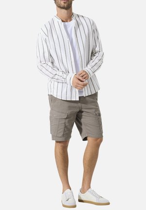 Man wearing white sneakers, light gray cargo shorts, white T-shirt, and white button-up shirt with black vertical stripes.