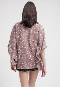 Kimono aperto con maniche fluide, caratterizzato da un motivo paisley bordeaux e crema su un tessuto leggero. L'orlo scende sotto la vita.