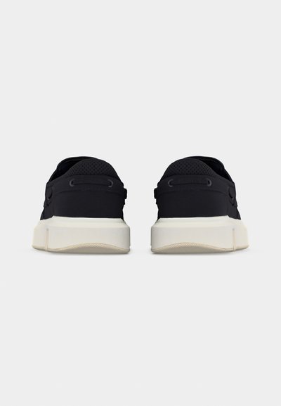 Vue arrière de baskets décontractées noires avec semelles épaisses blanches sur un fond clair uni.