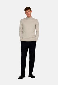 Light beige turtleneck sweater with a smooth, ribbed texture. Paired with dark trousers and black ankle boots, presenting a simple, classic look.