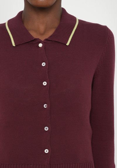 Cardigan en tricot bourgogne avec une texture côtelée, présentant un col vert clair contrastant et six boutons blancs sur le devant.