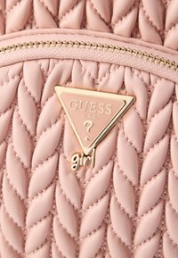 Mochila de cuero sintético rosa claro con diseño acolchado, herrajes dorados y una placa de logo triangular. Incluye la palabra "girl" en cursiva.