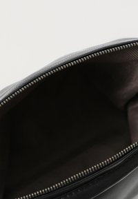 Interno di una borsa in pelle nera con una texture liscia, chiusura a zip lungo la parte superiore. La foderatura presenta un tessuto scuro e uniforme.
