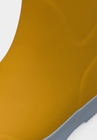 Κίτρινο λαστιχένιο γαλότσα με λεία υφή, στρογγυλεμένη κορυφή και λευκή σόλα. Ο σχεδιασμός έχει απαλές καμπύλες κατά μήκος του σώματος.