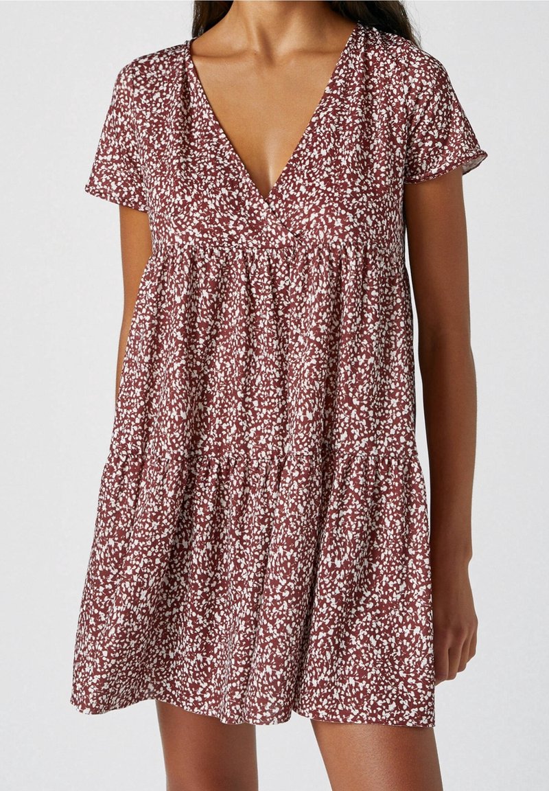 Vestido de estampado floral en rojo y blanco con escote en V y mangas cortas. Presenta un diseño en capas y un ajuste suelto y fluido.