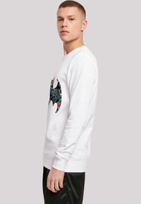 Hvid sweatshirt med et farverigt Batman-logo på brystet, rund halsudskæring, lange ærmer samt ribstrikkede manchetter og nederkant.