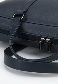 Bolso de cuero texturizado azul oscuro con cierre de cremallera, herrajes en tono plateado y una larga correa desmontable. Presenta detalles de costura en contraste.