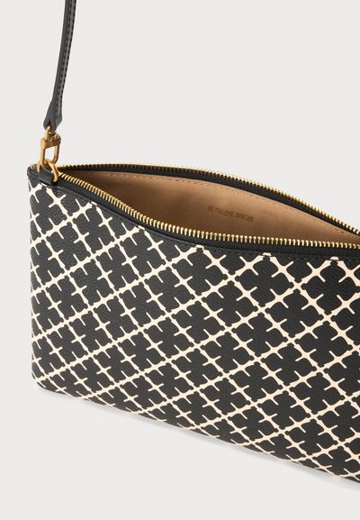 Pochette pour poignet à motifs noirs et blancs avec fermeture éclair dorée et sangle détachable, ouverte pour montrer la doublure intérieure en tissu beige.