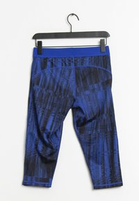 Niebieskie i czarne legginsy sportowe w wzory powieszone na czarnym wieszaku na białym tle.