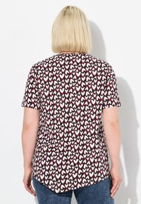 T-shirt à manches courtes en tissu à motifs avec de petits cœurs rouges et blancs sur un fond foncé. Ourlet arrondi, coupe décontractée.