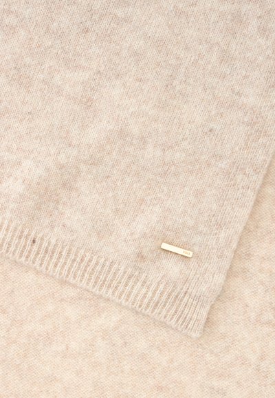 Tela de punto de lana beige con borde acanalado y pequeña etiqueta metálica rectangular grabada con "BOSS" en la esquina inferior.