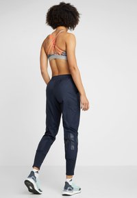 Sportoutfit met een grijze en neon oranje sport-bh en marineblauwe joggers met een strak ontwerp en zijkantdetails.