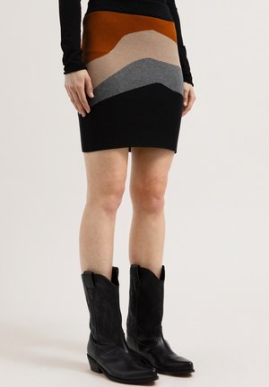 Mujer vistiendo una minifalda bicolor con secciones en negro, gris, beige y óxido, combinada con botas de vaquero negras.