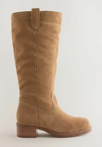 Ceļa augstuma bēšas zamšādas zābaki ar noapaļotu purngalu, dekoratīvām šuvēm un bloka papēdi. Aprīkoti ar cilpu augšpusē ērtai vilkšanai.