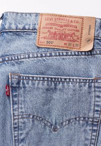 Světle modré džíny Levi's s kapsou na zadní straně, červený štítek Levi's a hnědá kožená etiketa ukazující velikost W32 L32 a model 501.