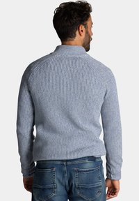 Gebreide trui in lichtblauw en wit, met een hoge kraag, geribbelde textuur en lange mouwen, gecombineerd met blauwe jeans.